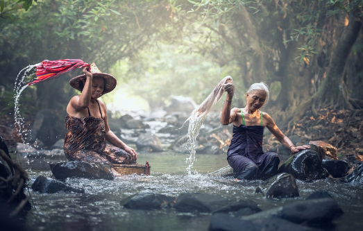 Kaks vana aasia naist  istuva jões kivi peal ja pesevad seal pesu.