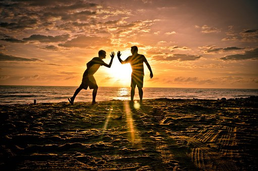 Kaks sõpra rannas päikeseloojangul teineteisele patsu löömas.